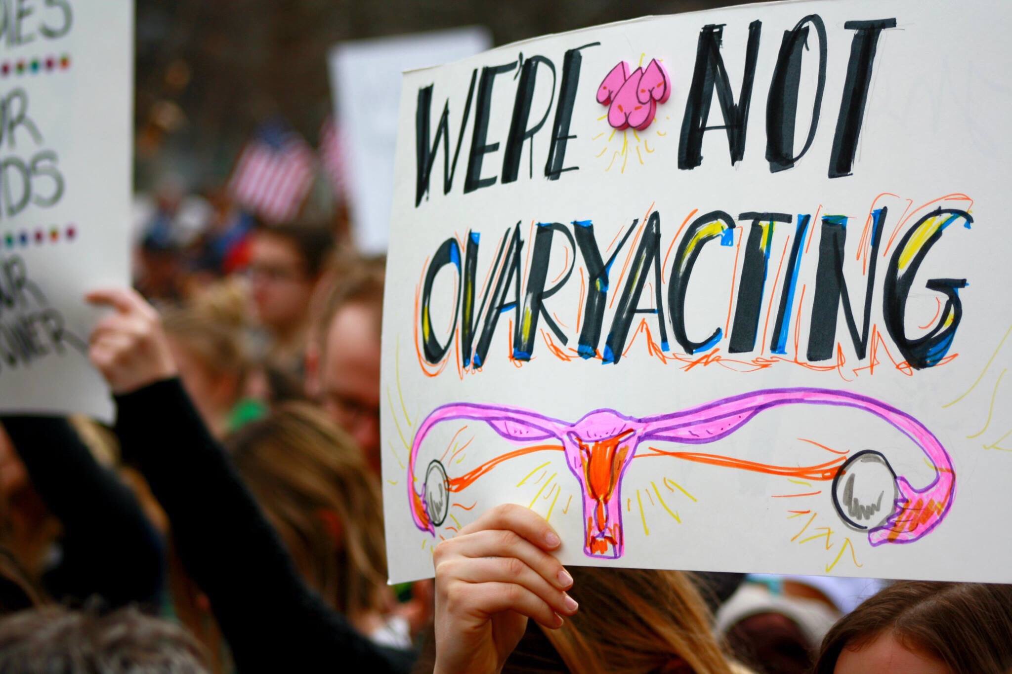 Photo of a hand holding up a sign that says "We're not ovaryacting"