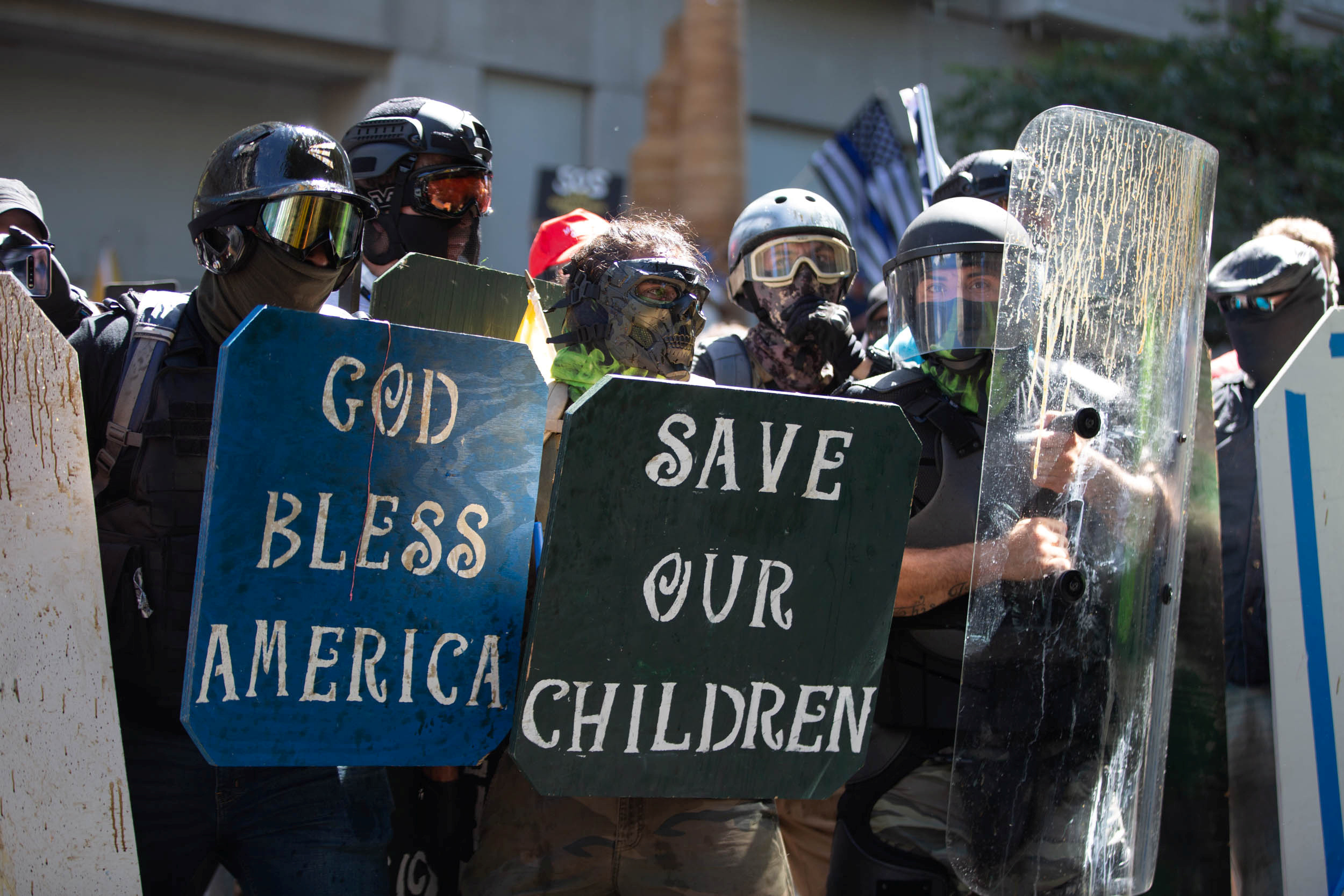 Photo of protestors holding up riot shields and signs that say "God Bless America"