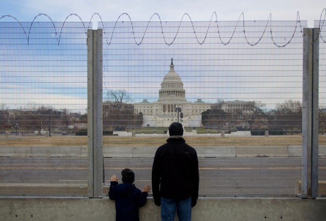 Photo of a man and child standing in front of a gate around the Capitol.
