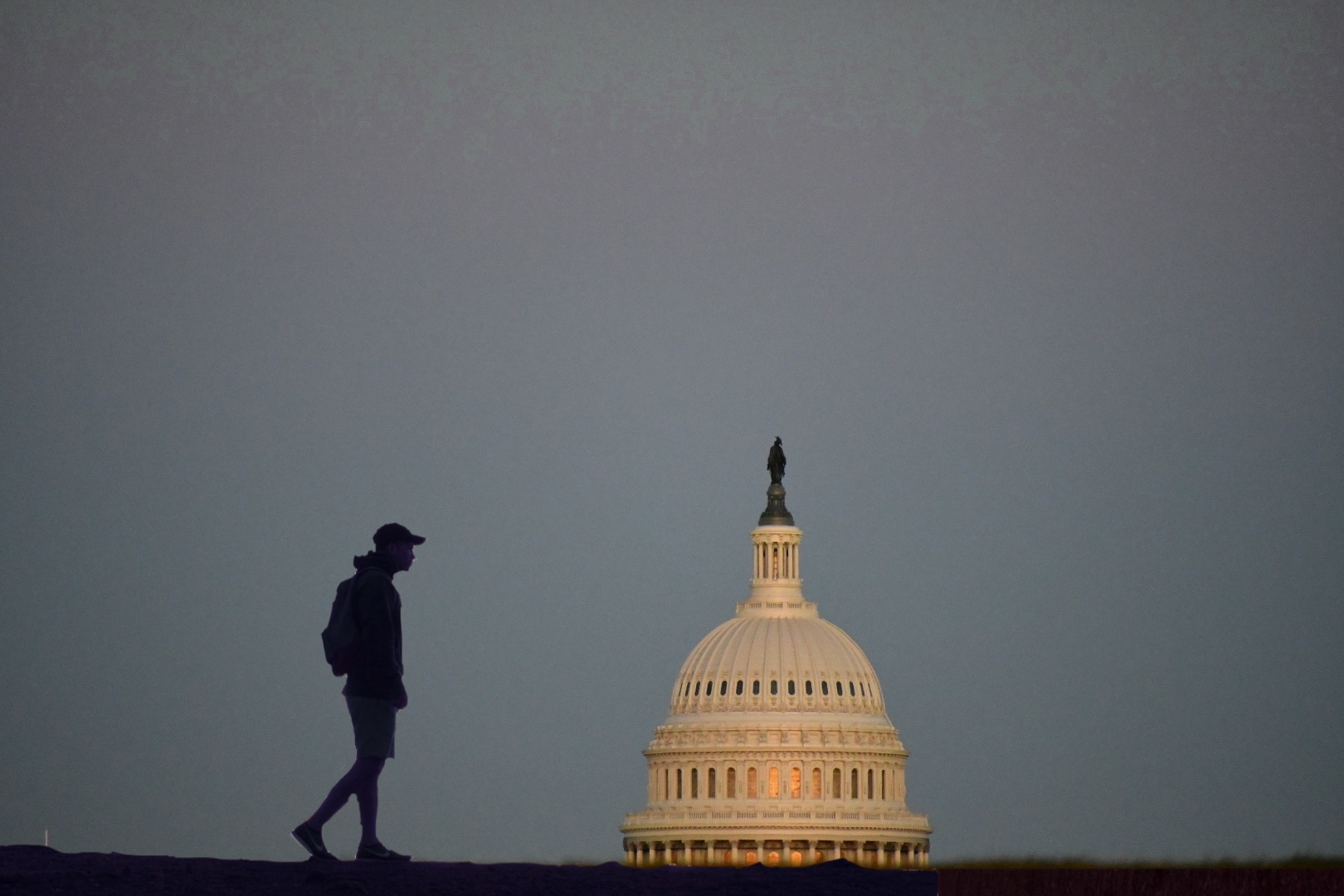 Photo of the dome of the capitol. Beside it, is the silhouette of a hiker.