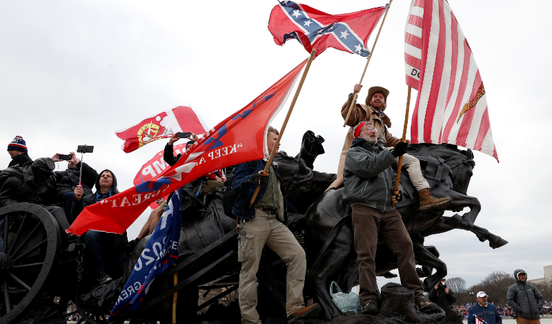 A crowd of protestors atop of a monument, waving confederate flags and Trump flags