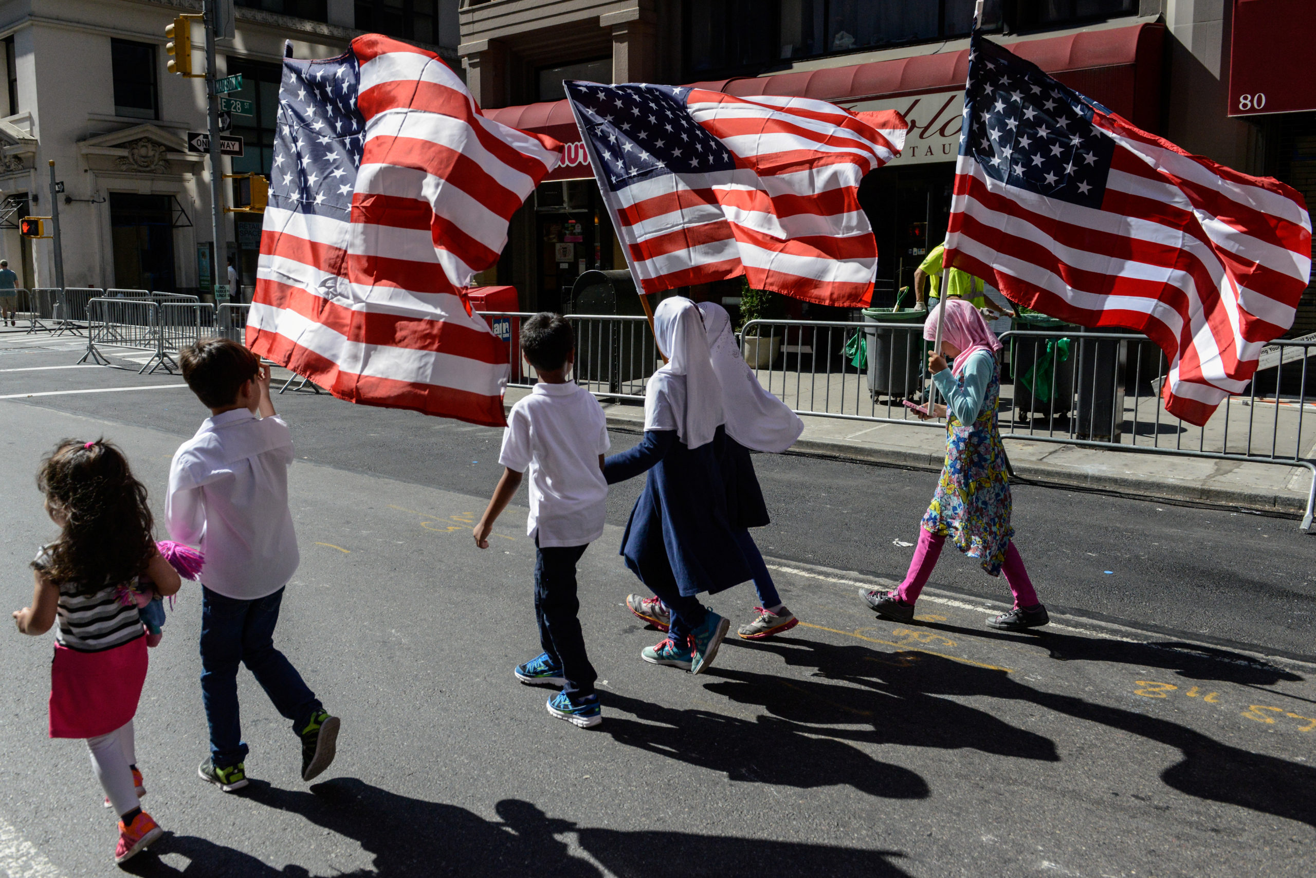 Photo of children holding American flags. There are six children, four are girls, three of the girls are wearing hijab.