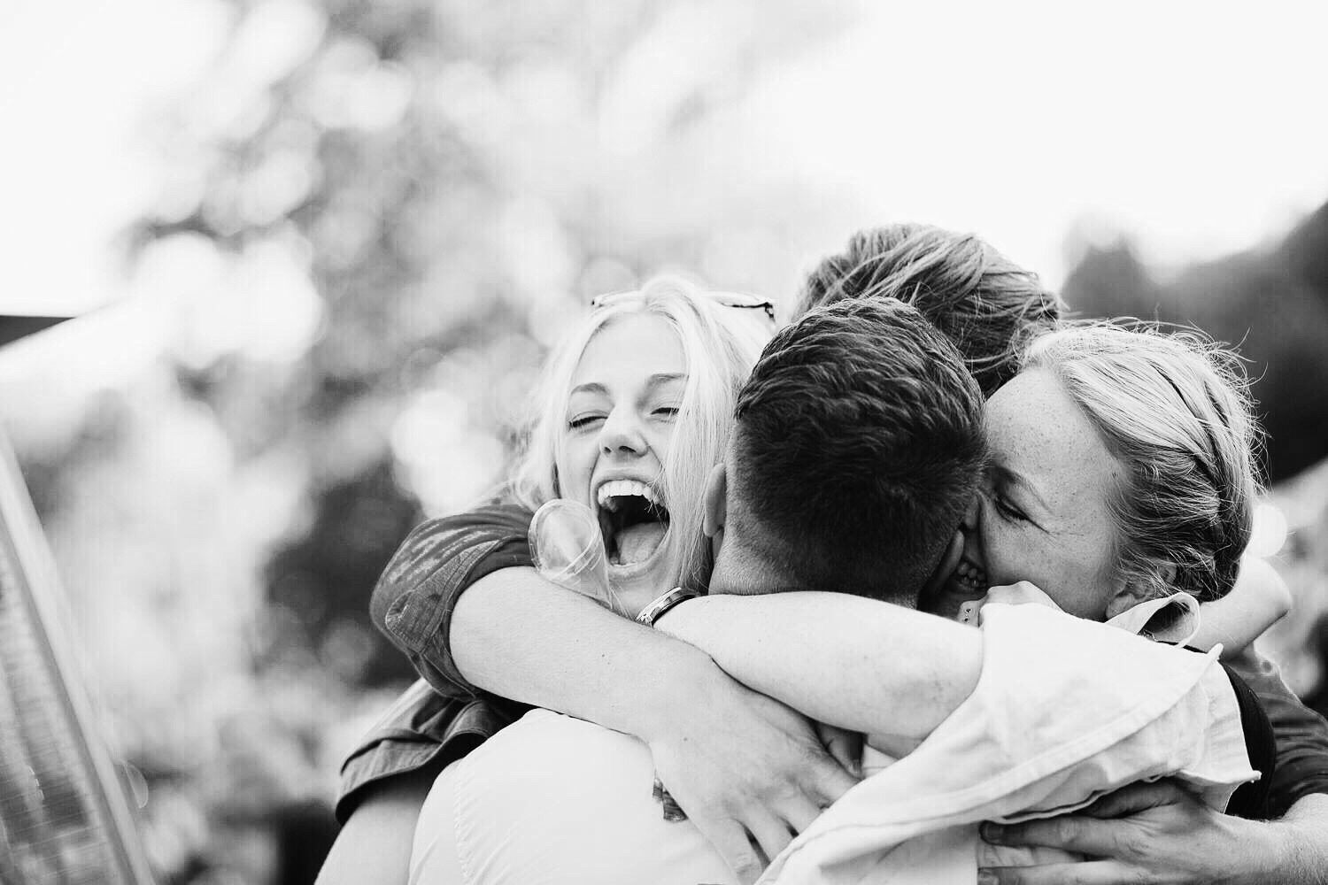 A black and white image shows four friends embracing with excitement