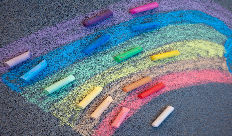 A rainbow drawn in chalk on asphalt, surrounded by chalk.