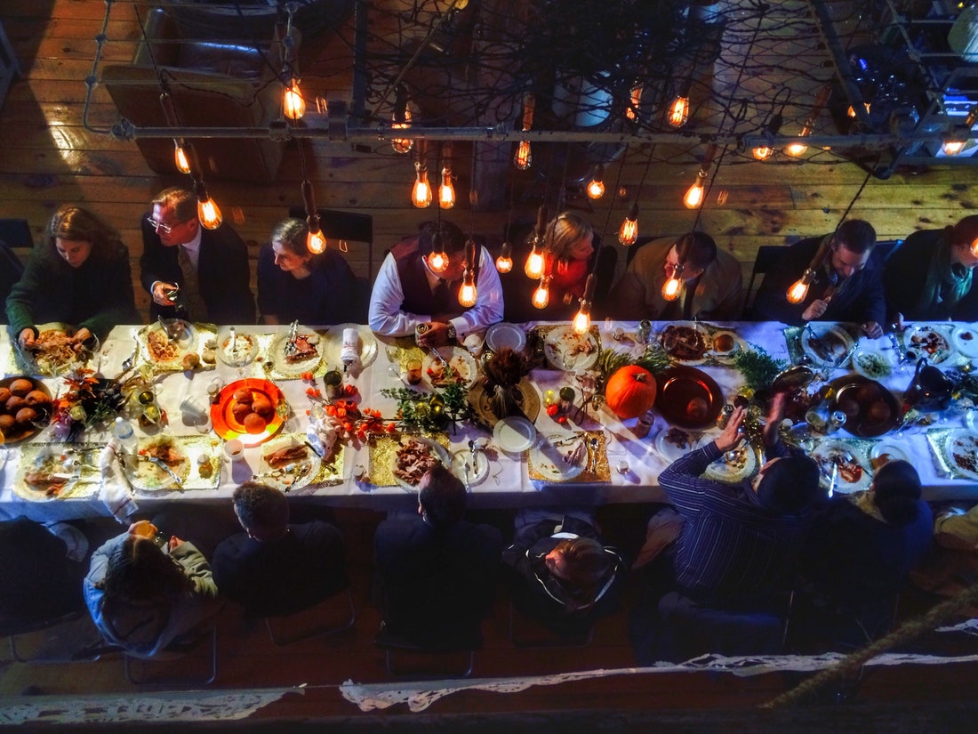 An overhead picture of a long, dimly-lit table set for Thanksgiving dinner. People sit at the table.