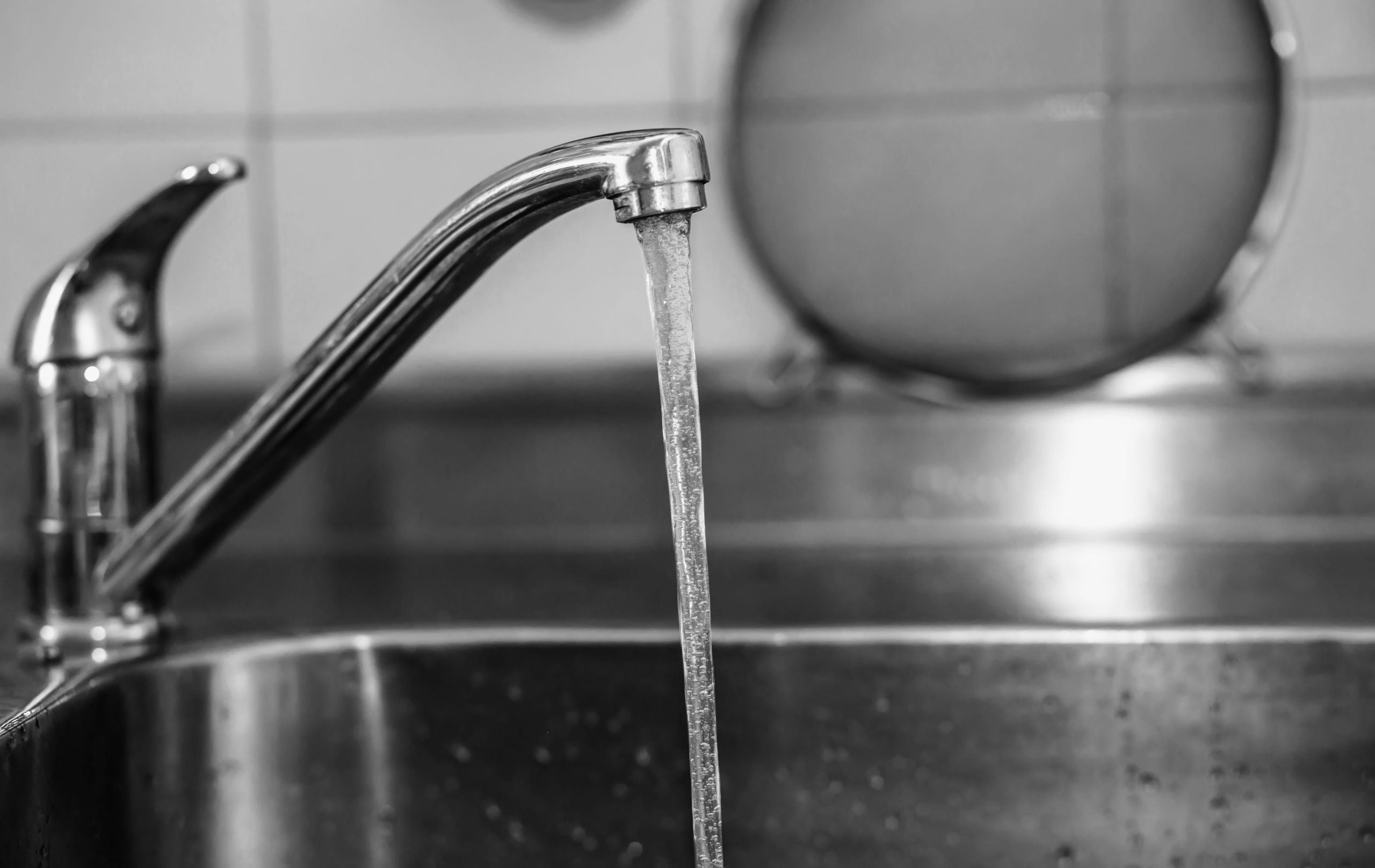 A black and white image of a running sink tap.
