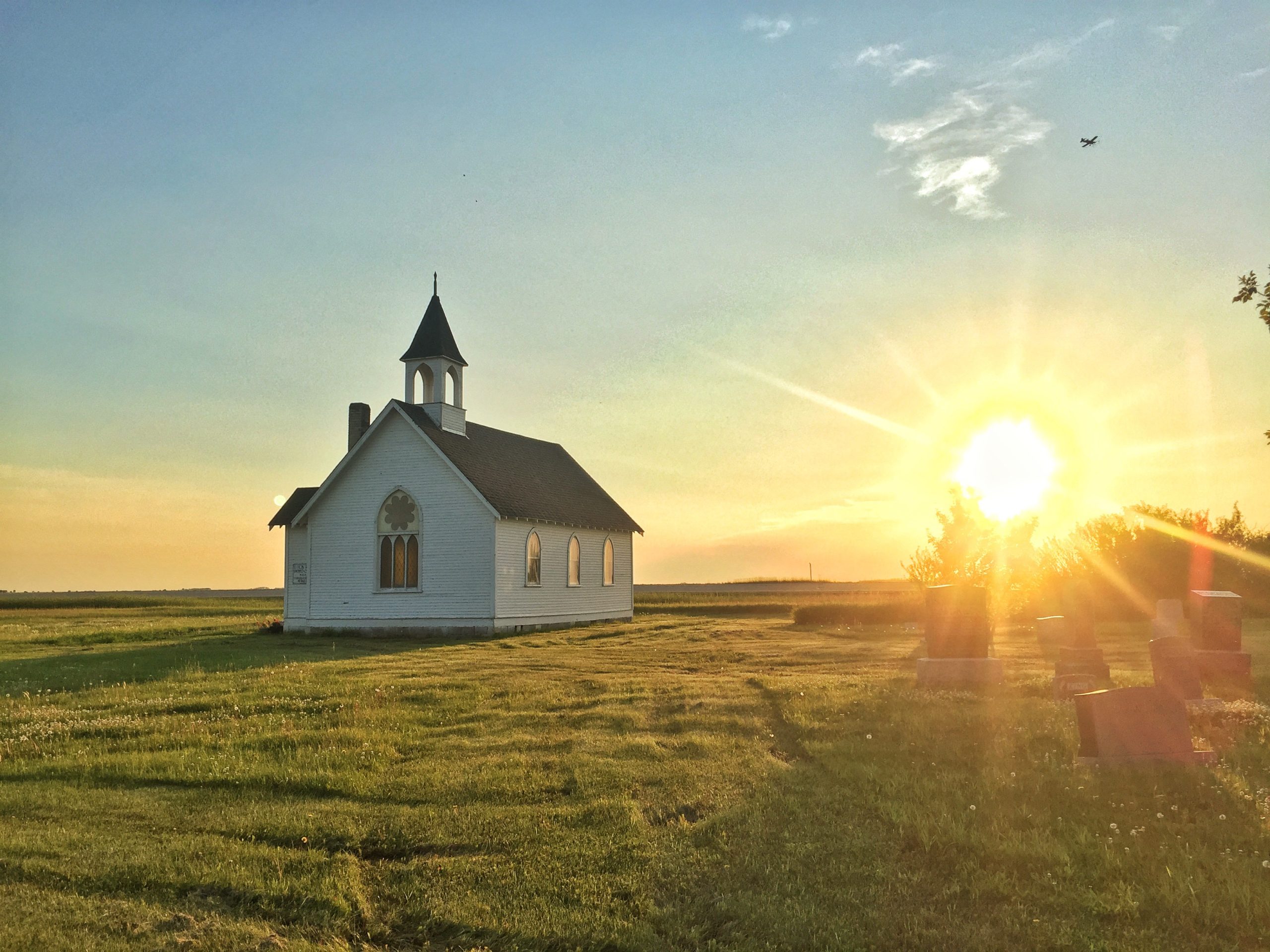 A little church on a prairie field as the sun rises over the horizon.
