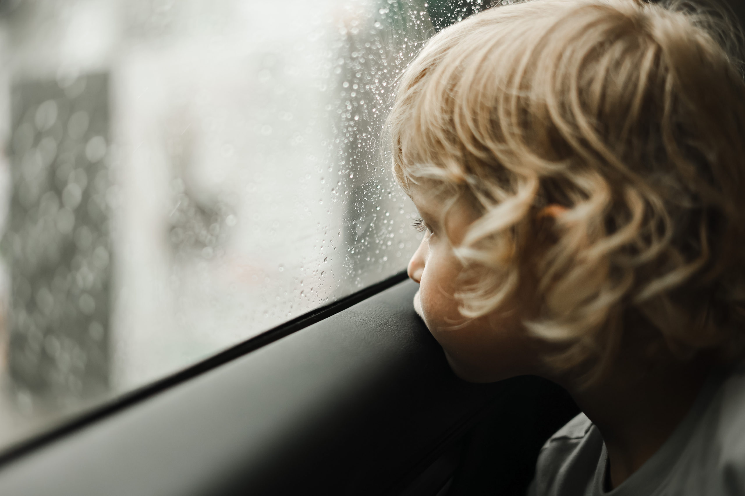 A child looks through a window of a car on a rainy day.
