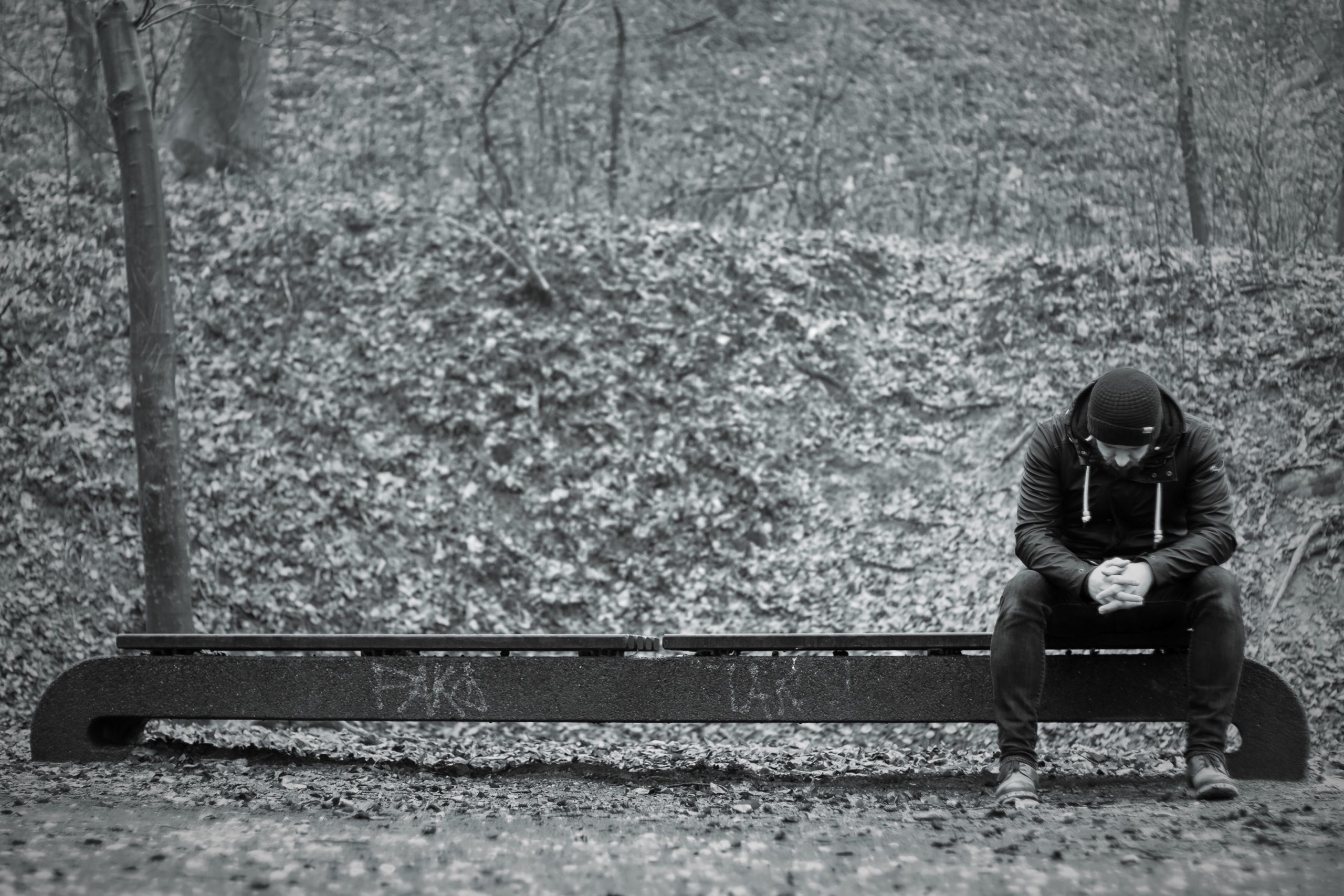 A black and white picture of single man sitting on a bench looking distraught.