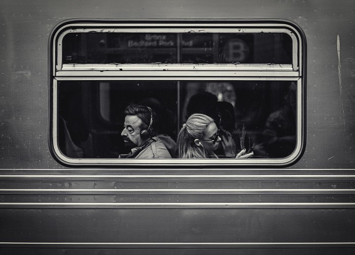 A black and white photo of a man and woman sitting back-to-back in a train car.