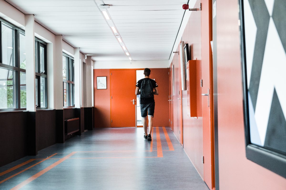 A student walks through an empty school hallway with orange walls.