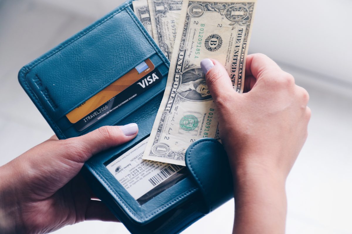 A woman's hands holding an open wallet. She has pulled out a one dollar bill.
