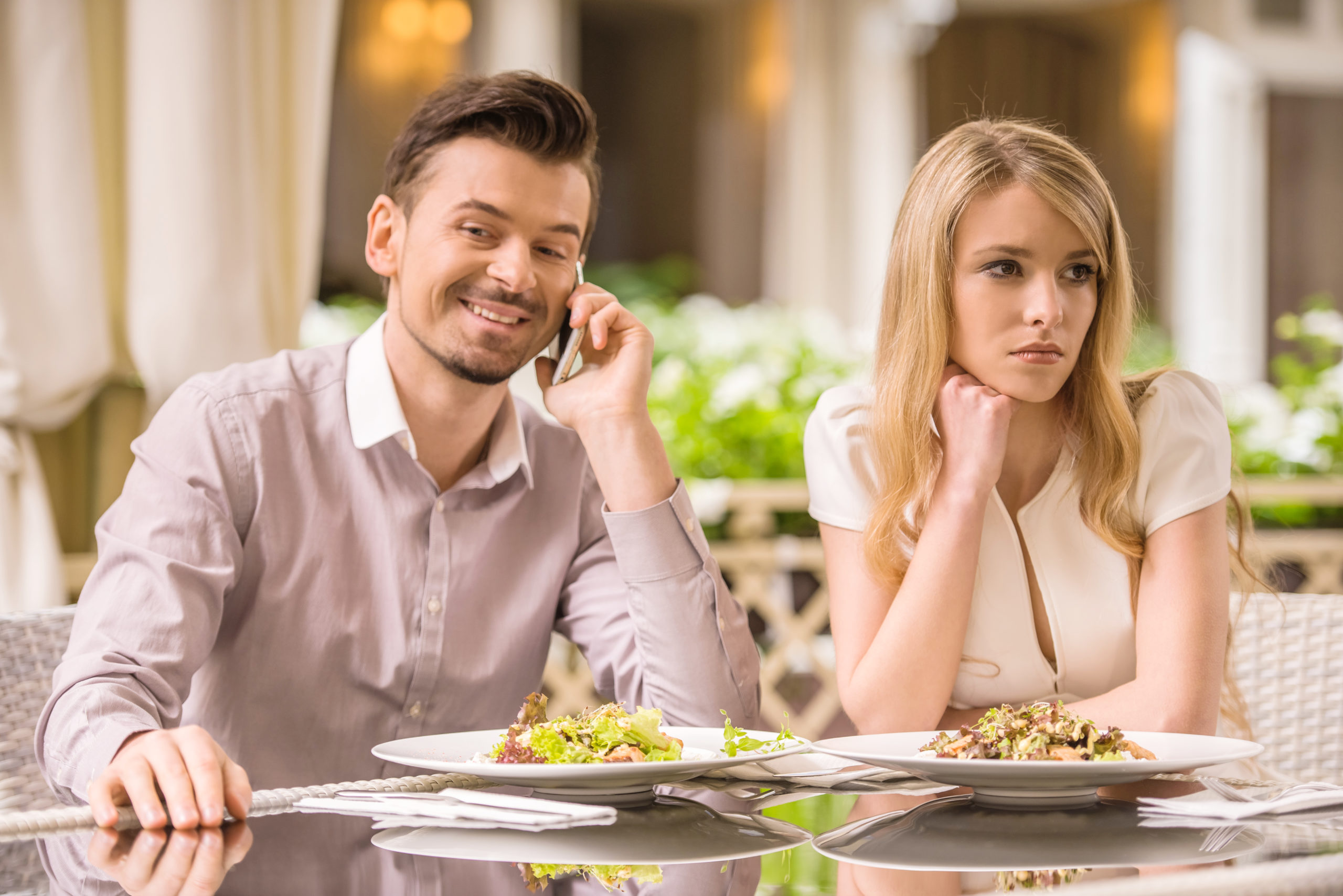 Woman is getting bored in restaurant while her boyfriend is talking on the phone.