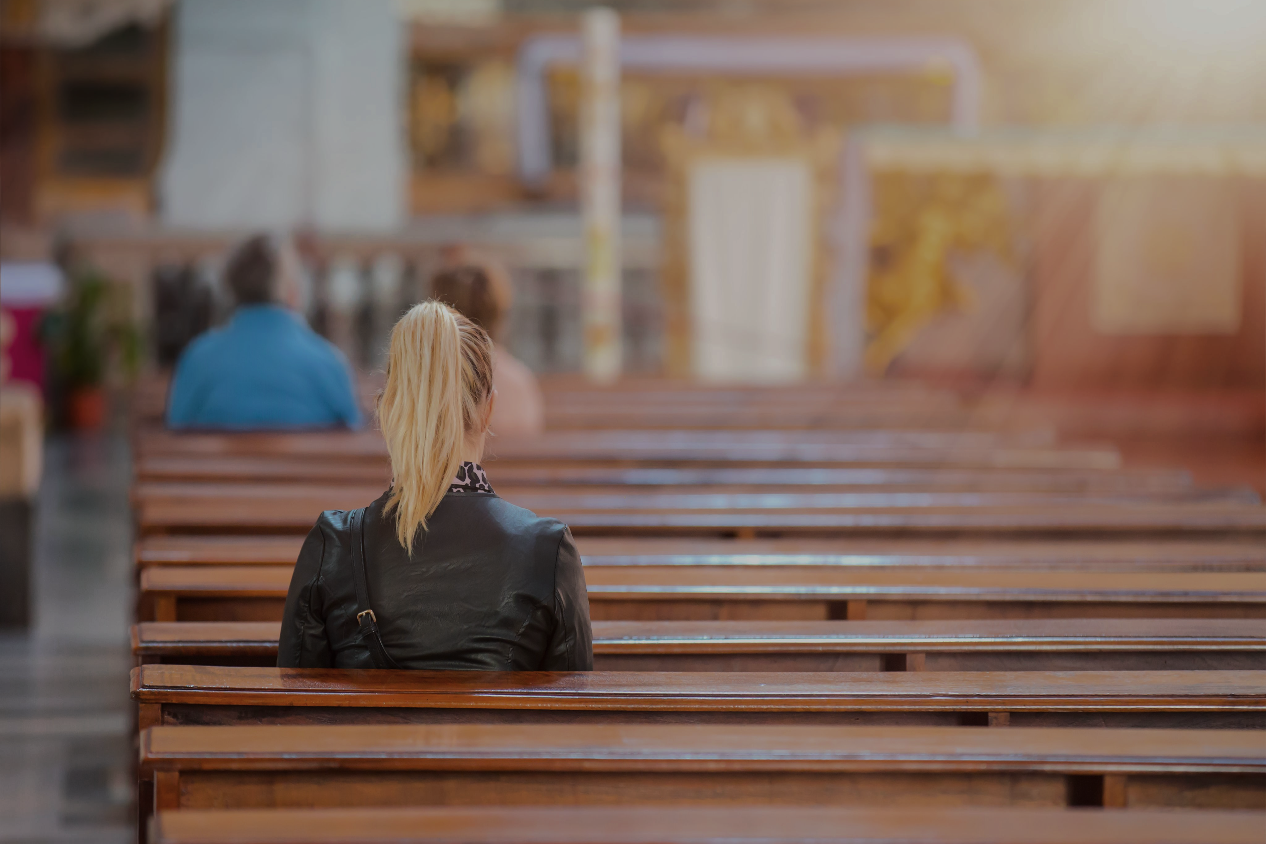 Photo of a woman sitting in the pews of a church with her back to the viewer