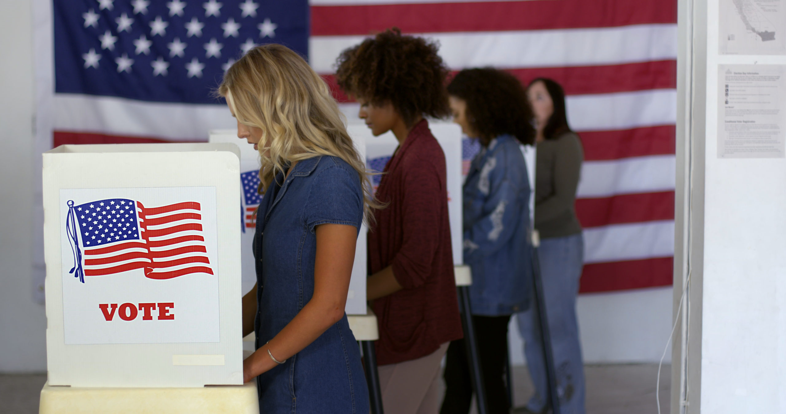 Young women voting in a row in front of American flag
