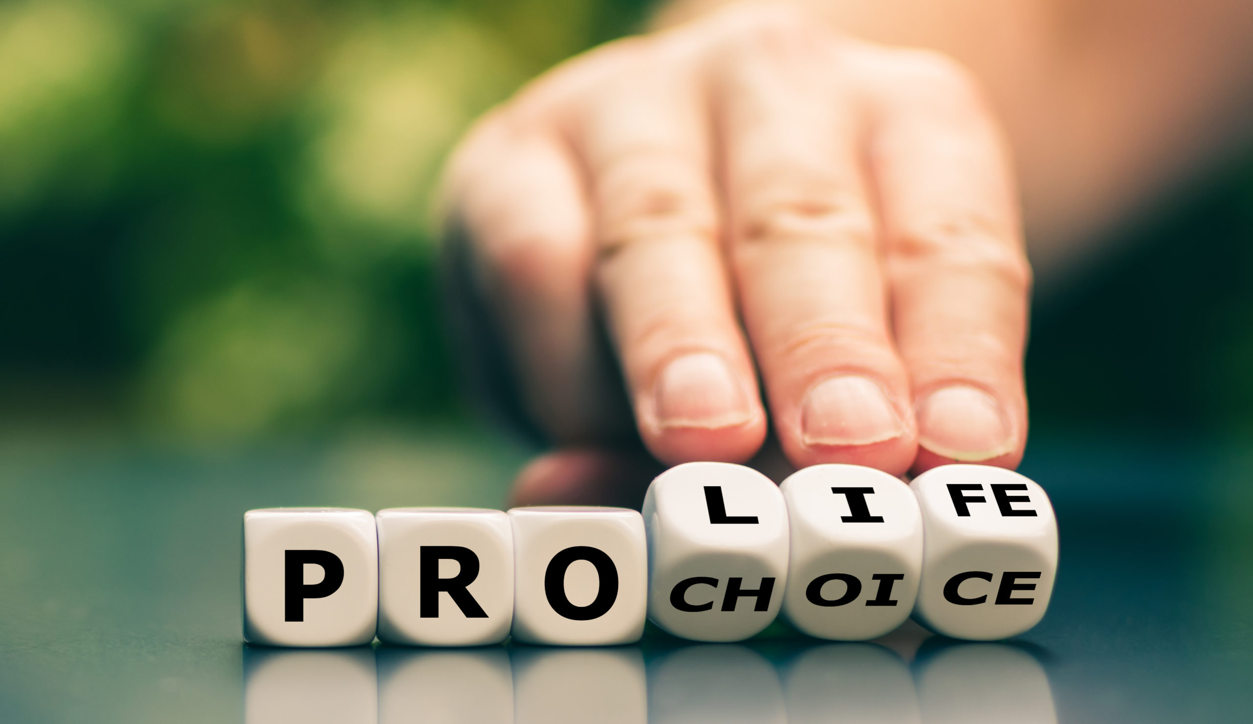 Six dice with the letters P R O L I F E C H O I C E they spell Pro Life and Pro Choice.