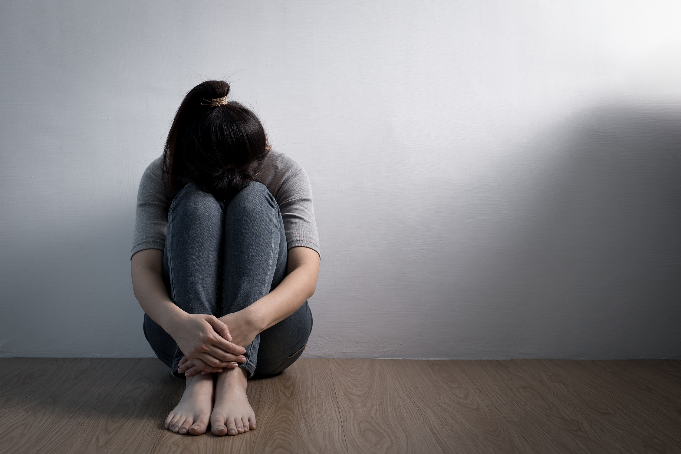 Photo of a girl sitting on the floor with her head between her knees.