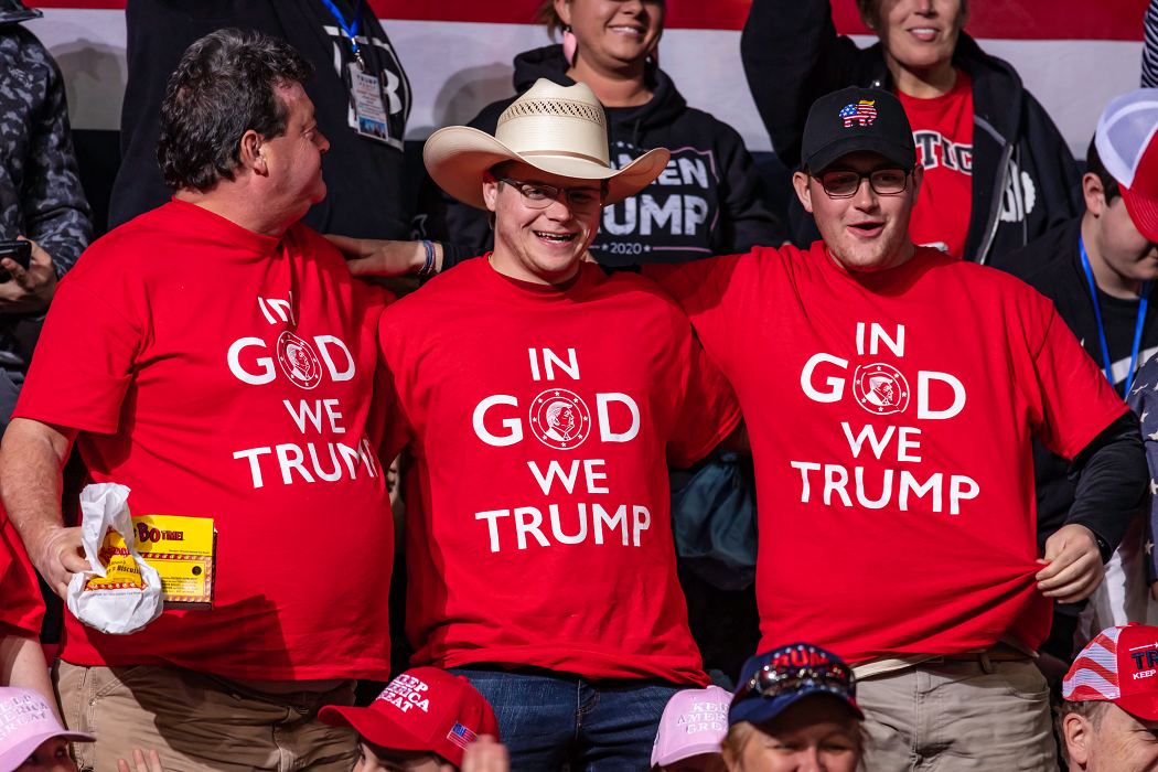 Three white men at a Trump rally wearing red "In God we Trump" t-shirts.